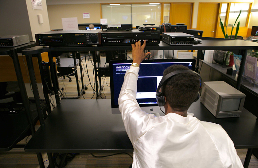 A person at a audio/video work station desk wearing headphones and making adjustments to AV hardware hooked up to the desk computer.